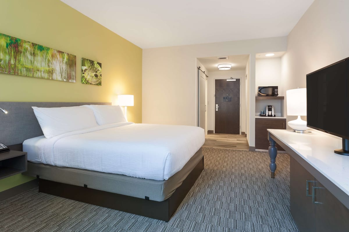 A hotel room with a bed, a desk, a TV, and a microwave.
