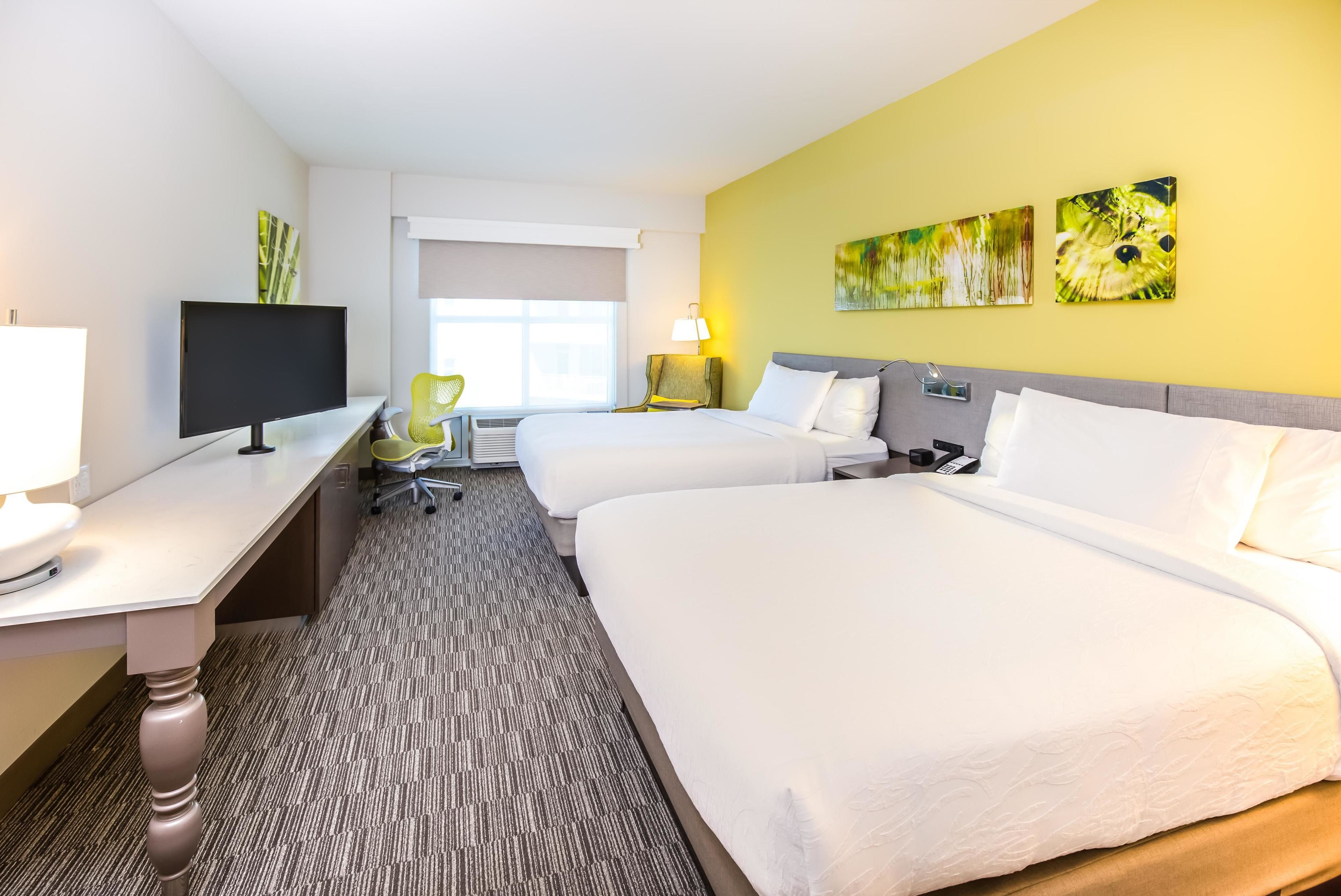 Een hotelkamer met een groot bed, een bureau met een computer, een stoel en kunstwerken aan de wanden.
