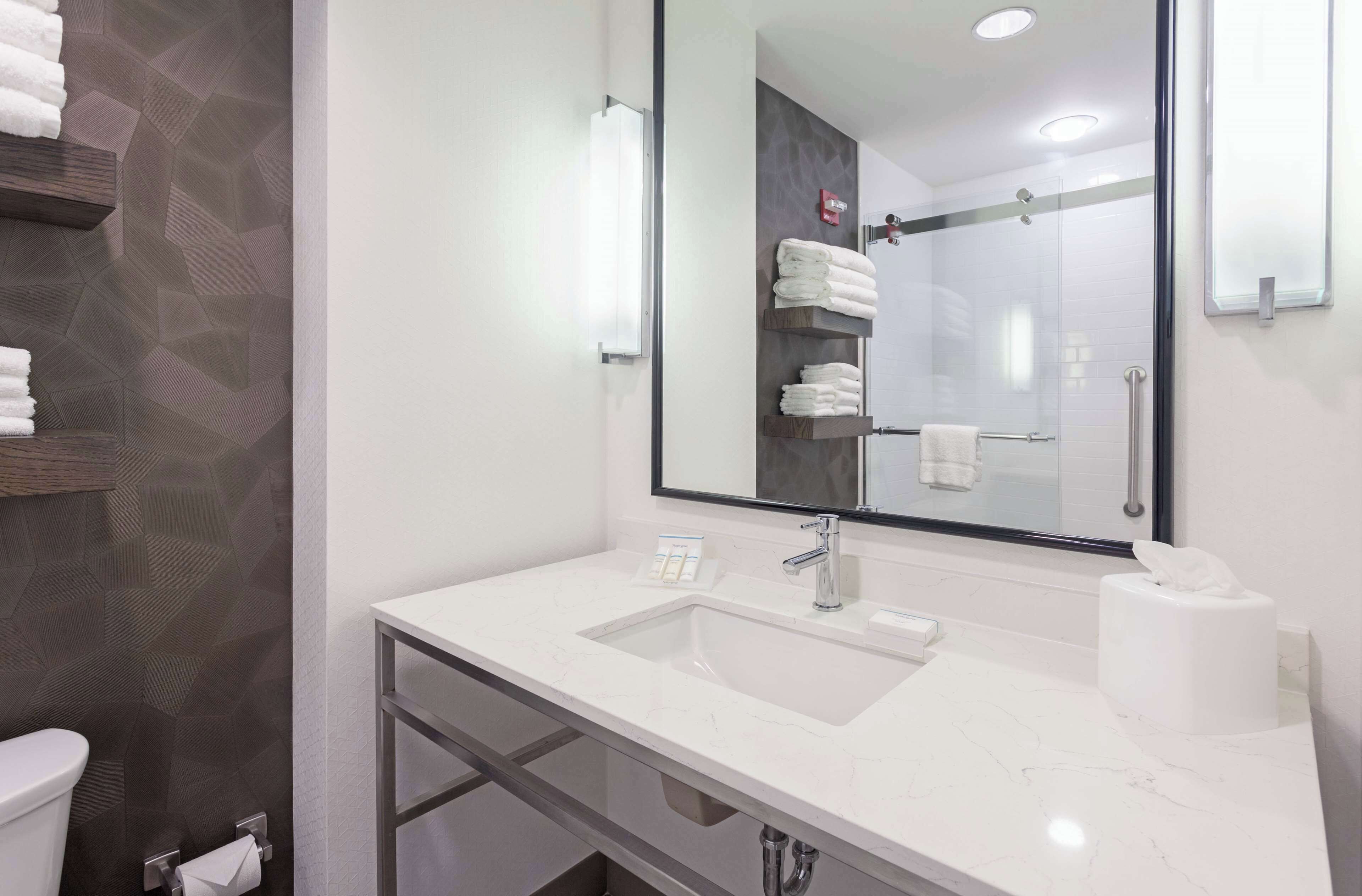 A modern bathroom with a white marble sink, a large mirror, and a glass shower enclosure.