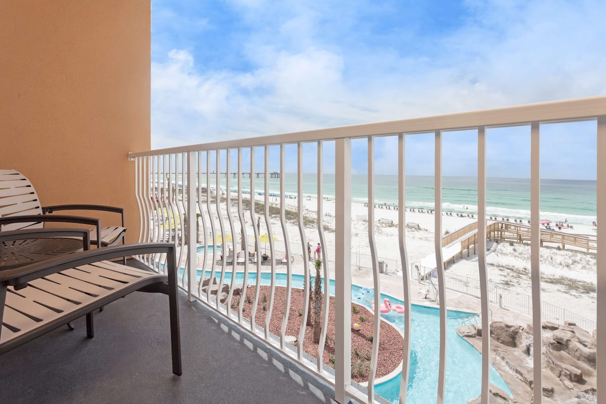 A balcony with a view of a beach, a pool, and a pier.