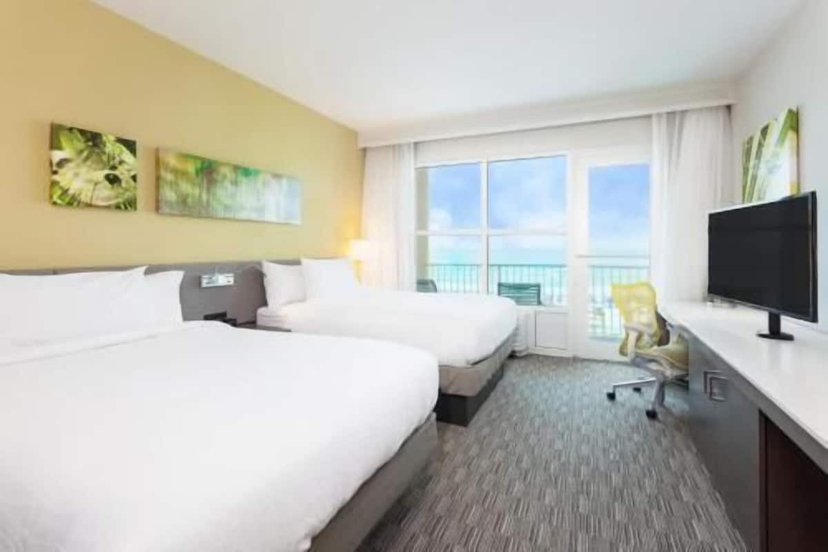 A hotel room with two beds, a TV, a chair, and a balcony with a view.
