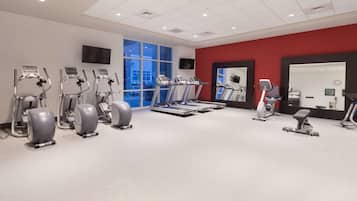 Un gimnasio con cintas de correr, elípticas y una máquina de remo.