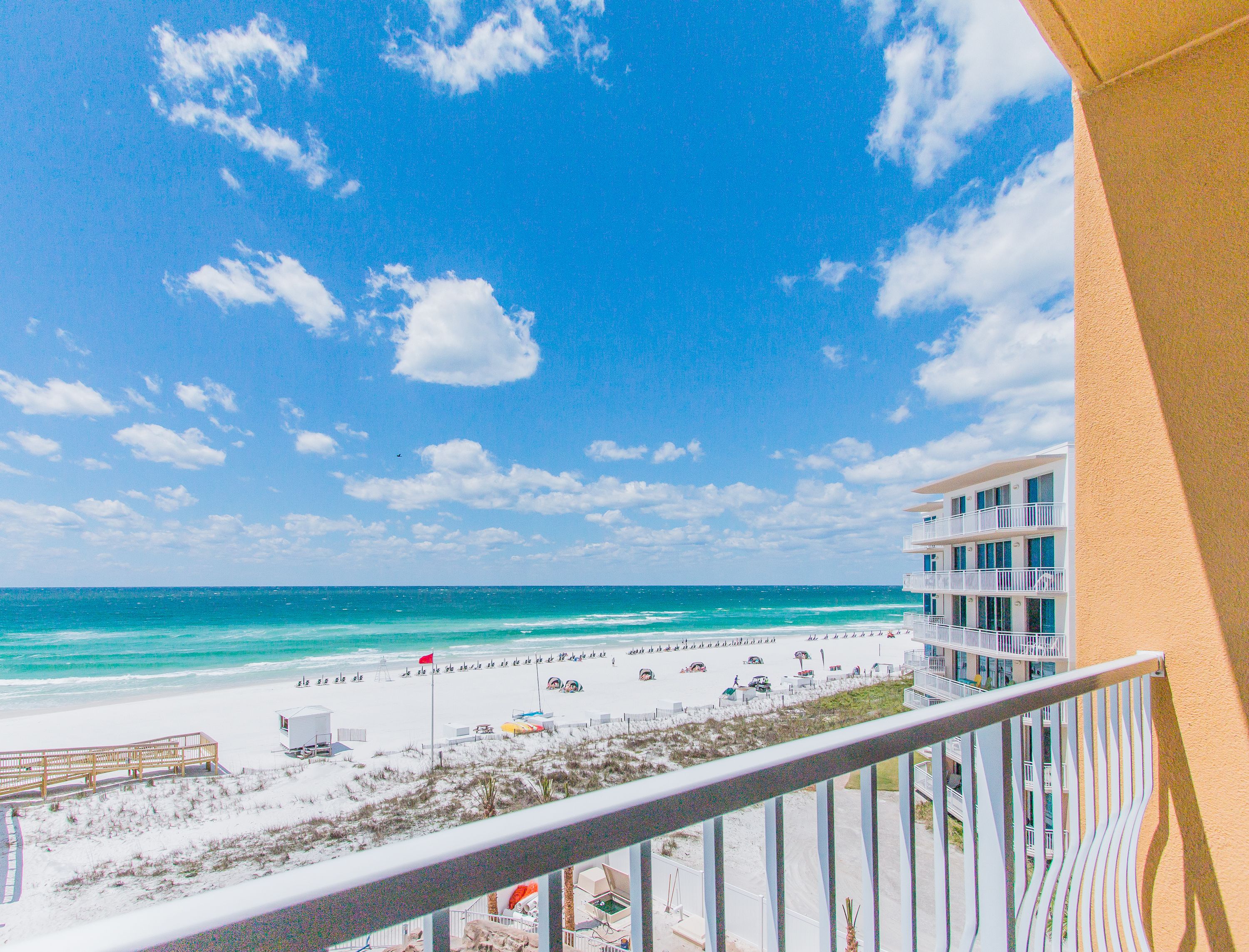 A beach view from a balcony overlooking a sandy beach with a clear blue sky.
