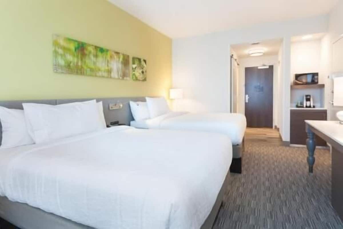 A hotel room with two beds, a desk, and a bathroom visible through an open door.