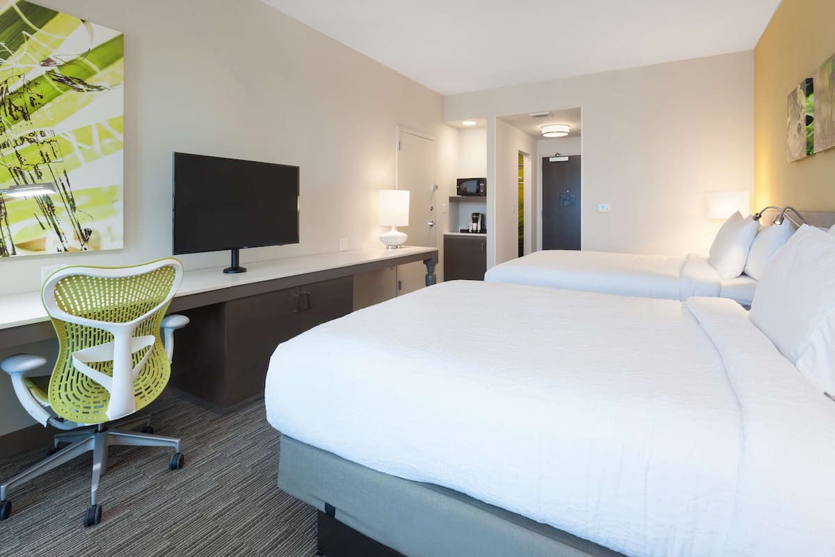 A hotel room with a bed, a desk with a chair, a TV, and a painting on the wall.
