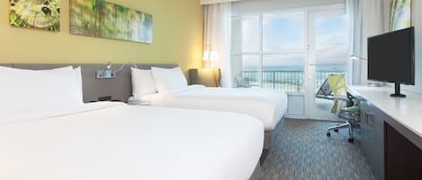 A hotel room with two beds, a desk, a TV, and a balcony with a view.