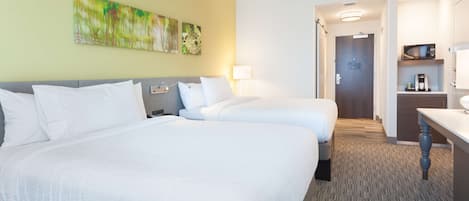 A hotel room with two beds, a desk, a lamp, and a painting on the wall.