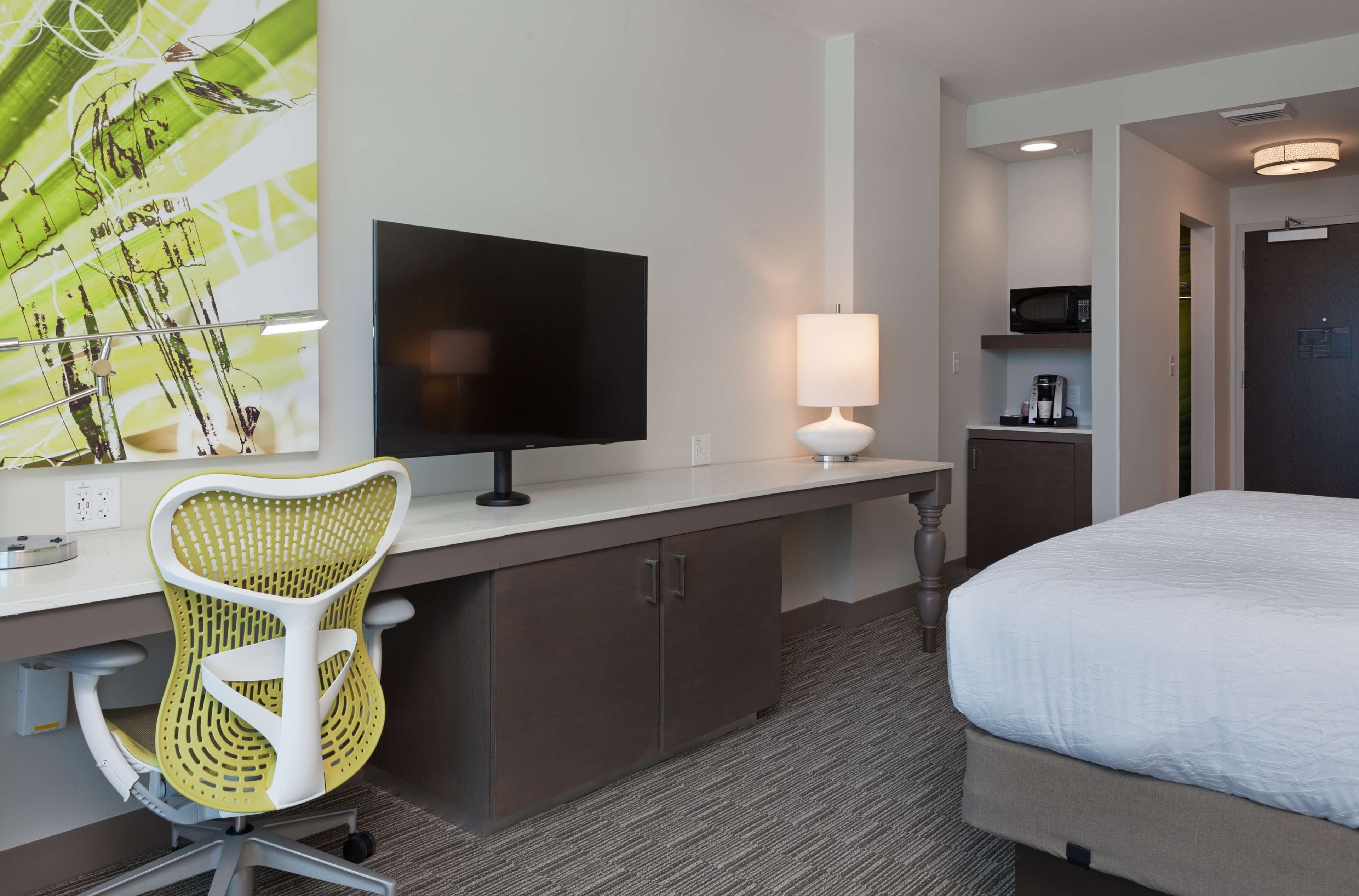 A hotel room with a bed, a desk with a flat-screen TV, a chair, a lamp, and a microwave.