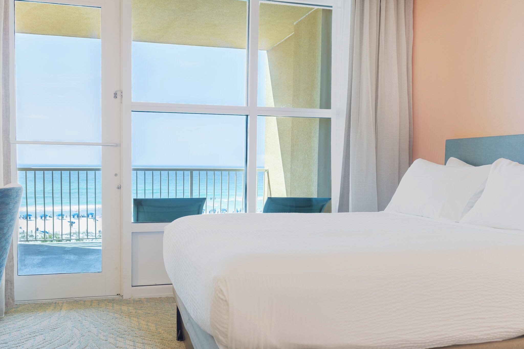 A hotel room with a bed, a view of the beach, and a balcony with a railing.