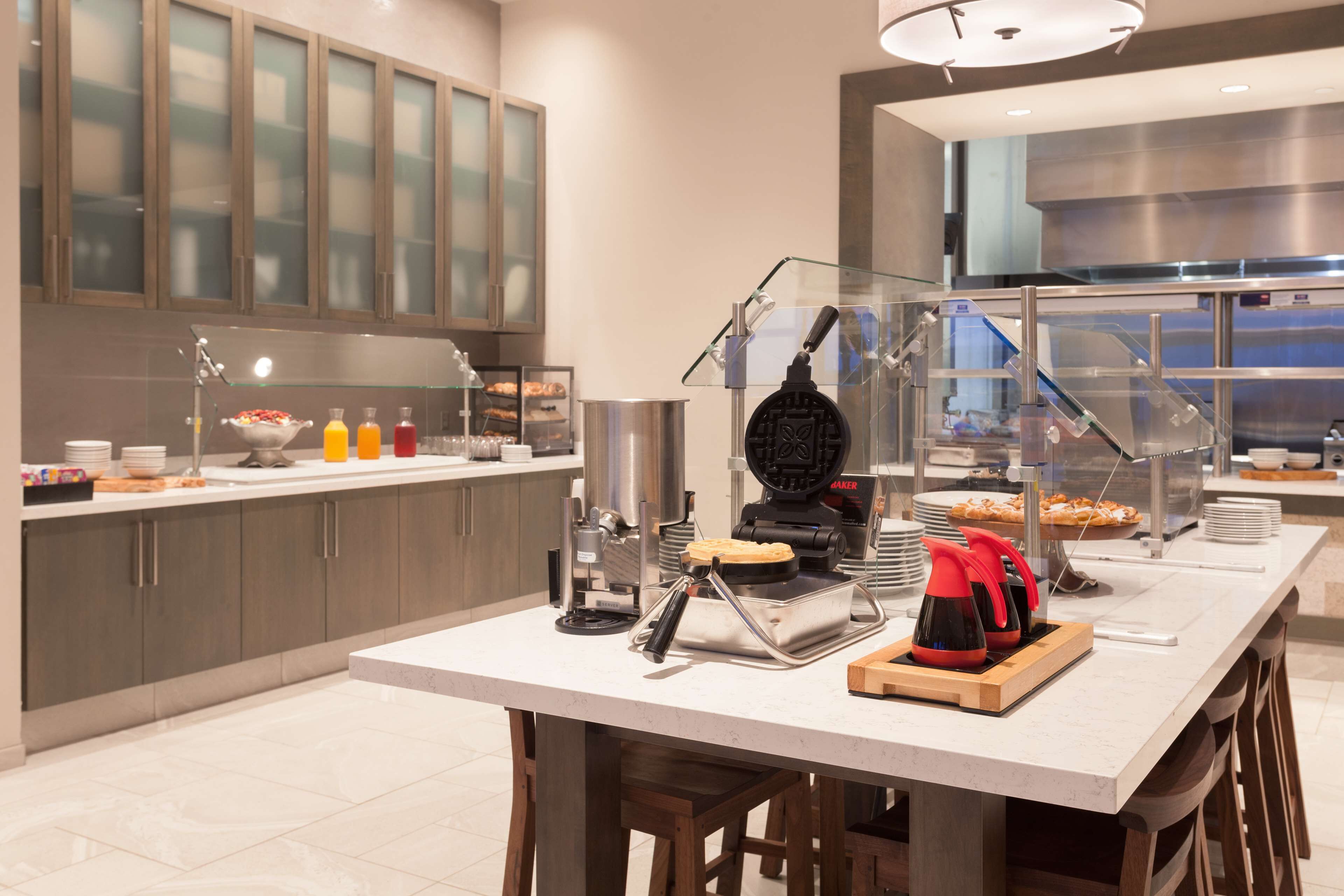 A modern kitchen with a buffet setup, including a waffle maker, a coffee machine, and various food items.