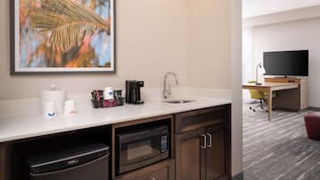 A compact kitchenette with a microwave, coffee maker, and sink. A flat-screen TV is mounted on the wall in the adjacent room.
