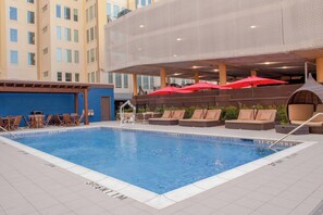 An indoor swimming pool with lounge chairs and umbrellas, surrounded by a modern building with multiple floors. - TownePlace Suites by Marriott Dallas Downtown (Dallas)