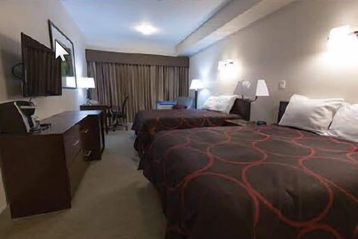 A hotel room with two beds, a desk, a chair, and a dresser.