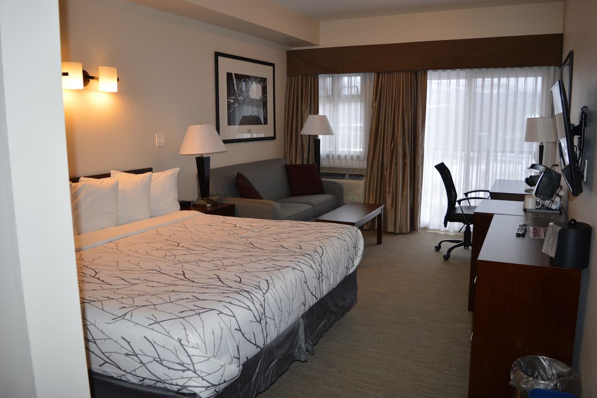 A hotel room with a large bed, a sofa, a desk with a chair, and a window with curtains.