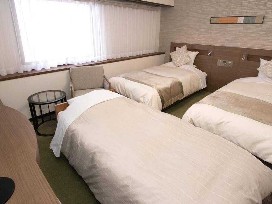 A hotel room with two single beds, a desk, and a window with curtains.
