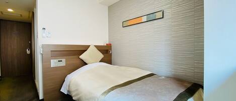 A hotel room with a single bed, a wooden headboard, a wall-mounted control panel, and a door leading to another room.
