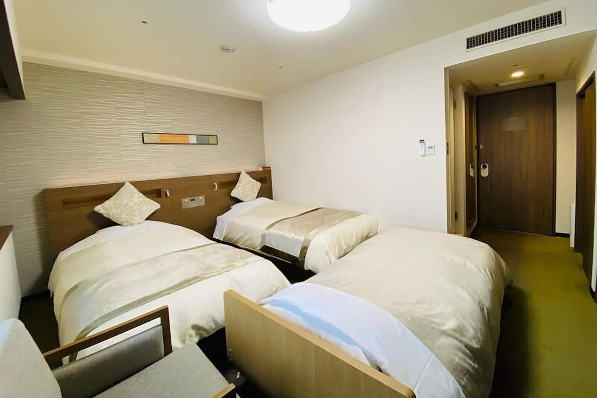 A hotel room with two single beds, a wooden headboard, a small table, and a door leading to a hallway.