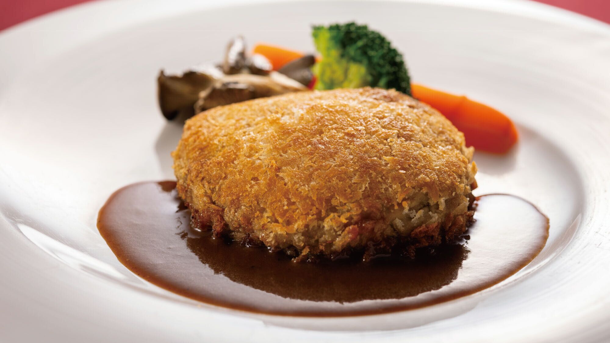 Un plat, probablement gratiné, avec une croûte dorée, accompagné d’un accompagnement de légumes et nappé d’une sauce foncée.