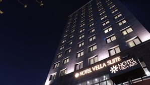 Een hoog hotelgebouw bij nacht met verlichte signage voor Vella Suite.