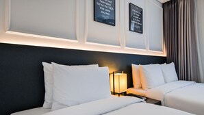 Een hotelkamer met twee bedden, een nachtkastje met een lamp en motiverende posters aan de muur.