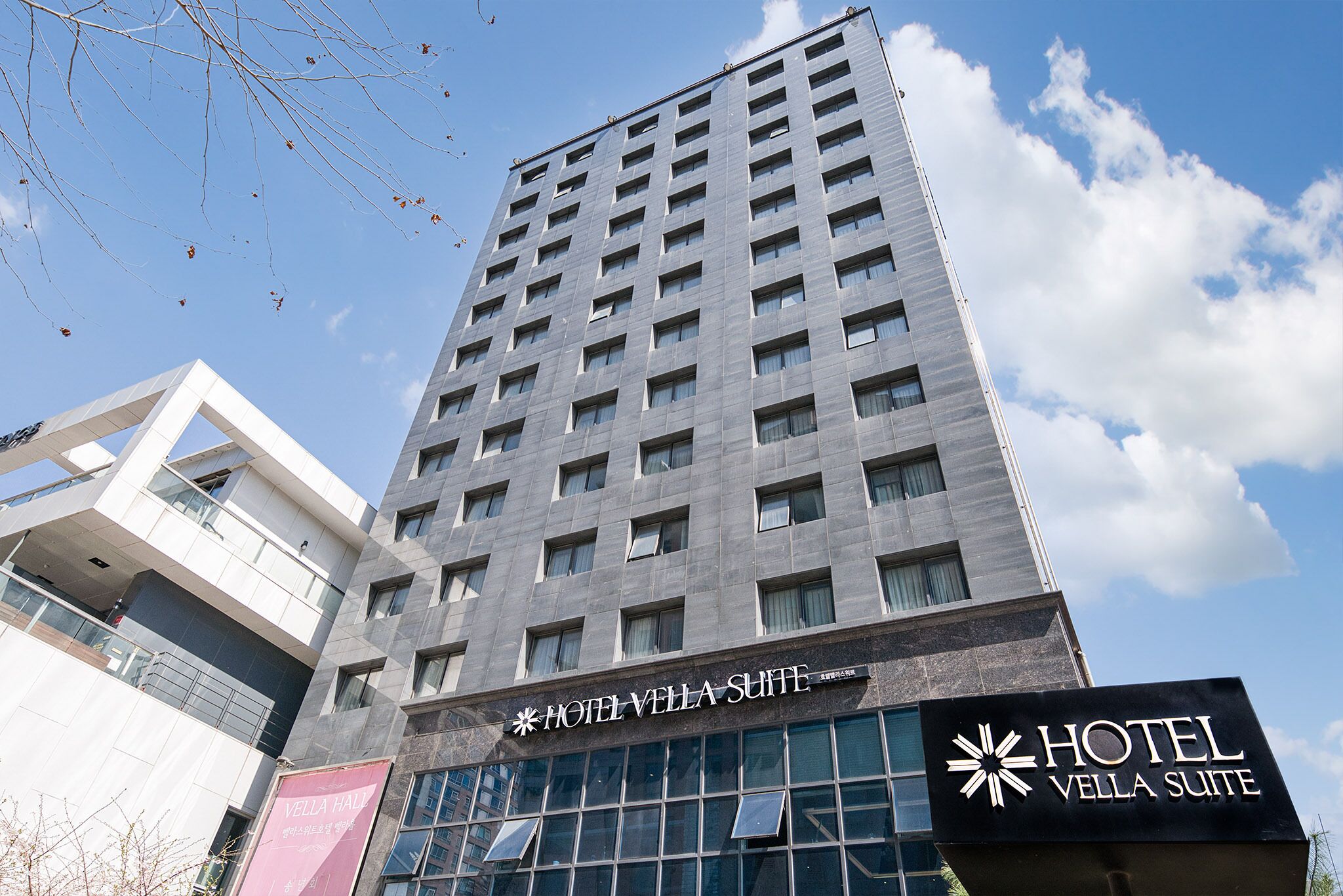A hotel building with multiple floors, large windows, and a prominent sign for the Hotel Vella Suite.