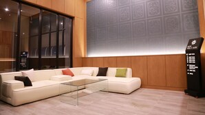 Een moderne hotel lobby met een hoekbank, een glazen salontafel en een muur met een geometrisch patroon.