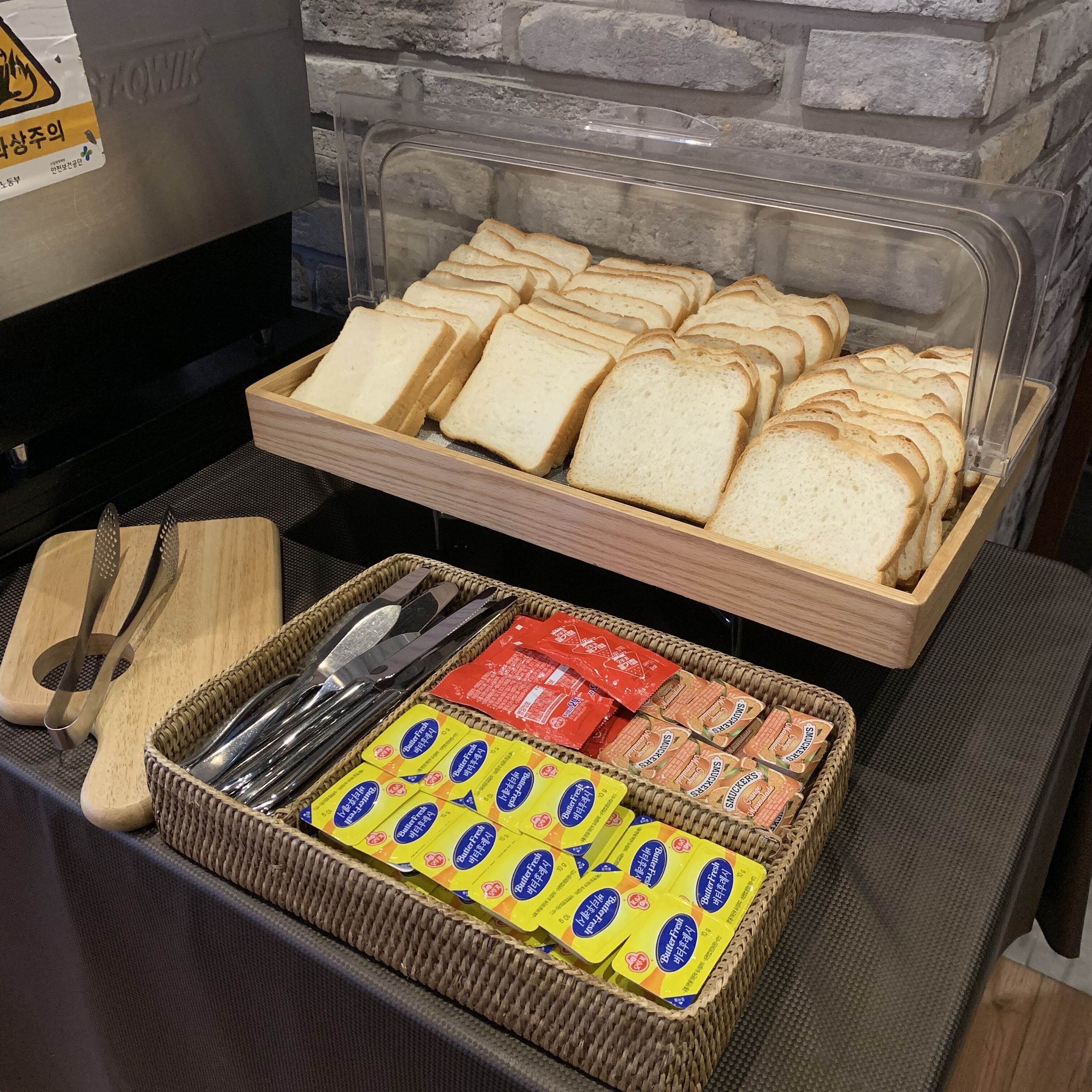 Un bufé de desayuno con pan en rodajas, mantequilla y porciones individuales de mermelada.