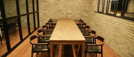 A conference room with a long wooden table and black chairs, brick walls, and large windows.