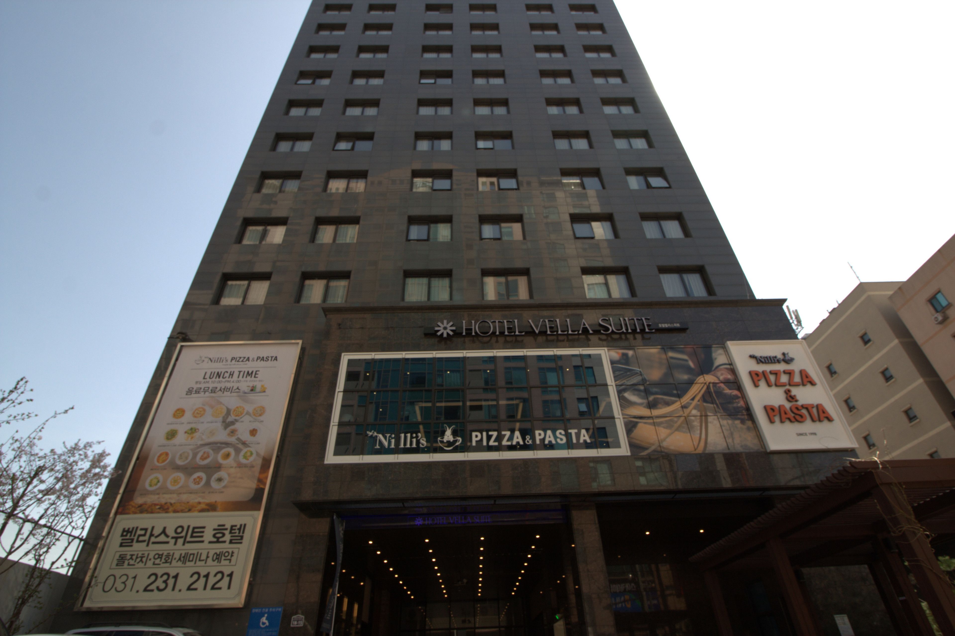 A tall building with a sign for 'Hotel Vella Suite' and 'Ni Illi's Pizza & Pasta' on the facade.