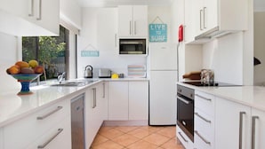 Een moderne keuken met witte kastjes, een magnetron, een koelkast en een spoelbak. Op de muur hangen decoratieve borden en op het aanrecht staat een schaal met fruit.