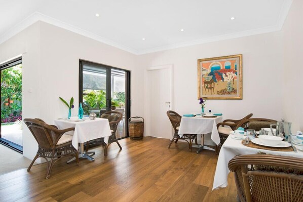 Un coin repas avec des chaises et des tables en osier, une grande fenêtre et un tableau accroché au mur.