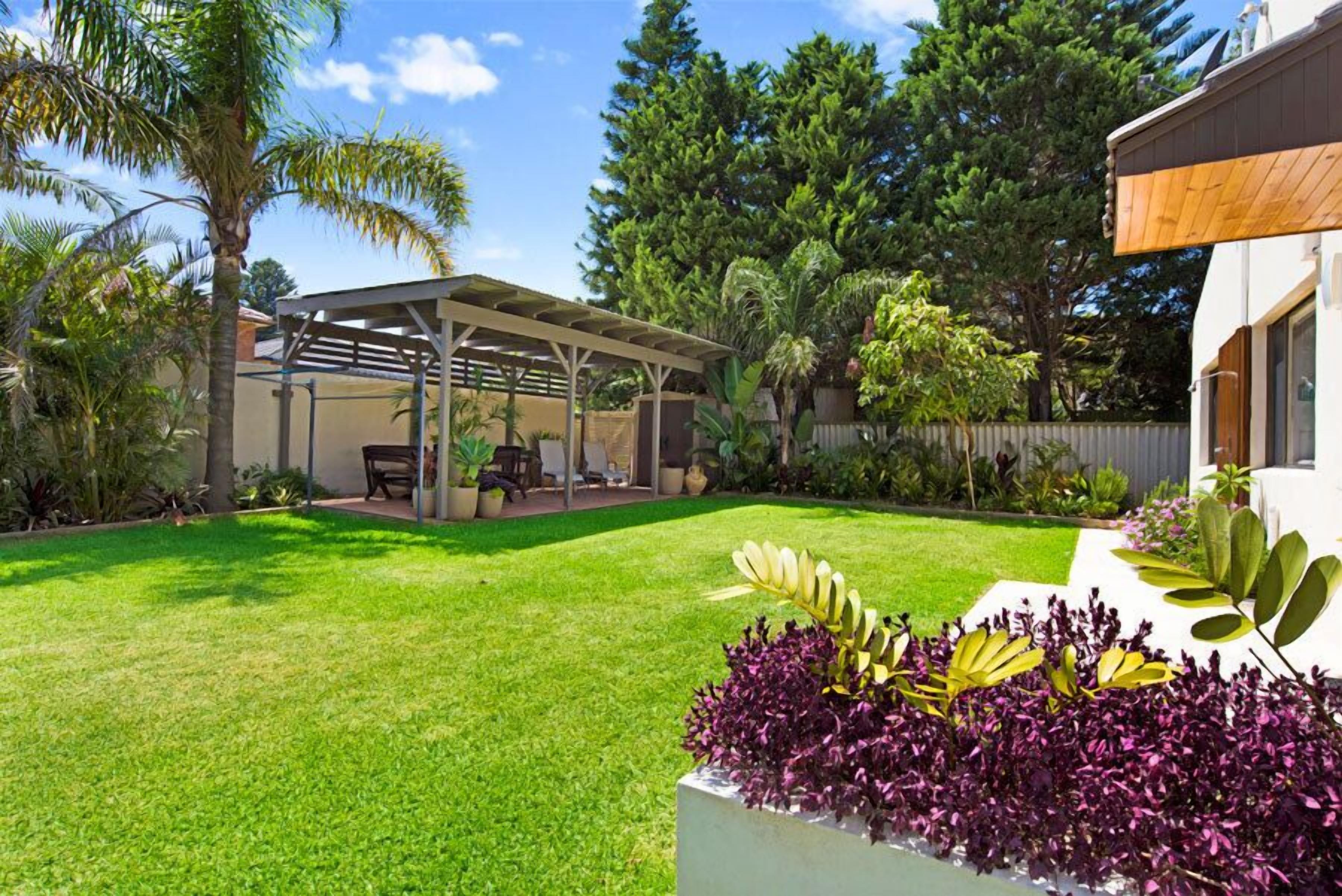 Un jardin arrière bien entretenu, doté d  ’un patio couvert, d’une végétation luxuriante et de diverses espèces de plantes.