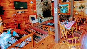 A cozy log cabin interior with a stone fireplace, wooden furniture, and a television.