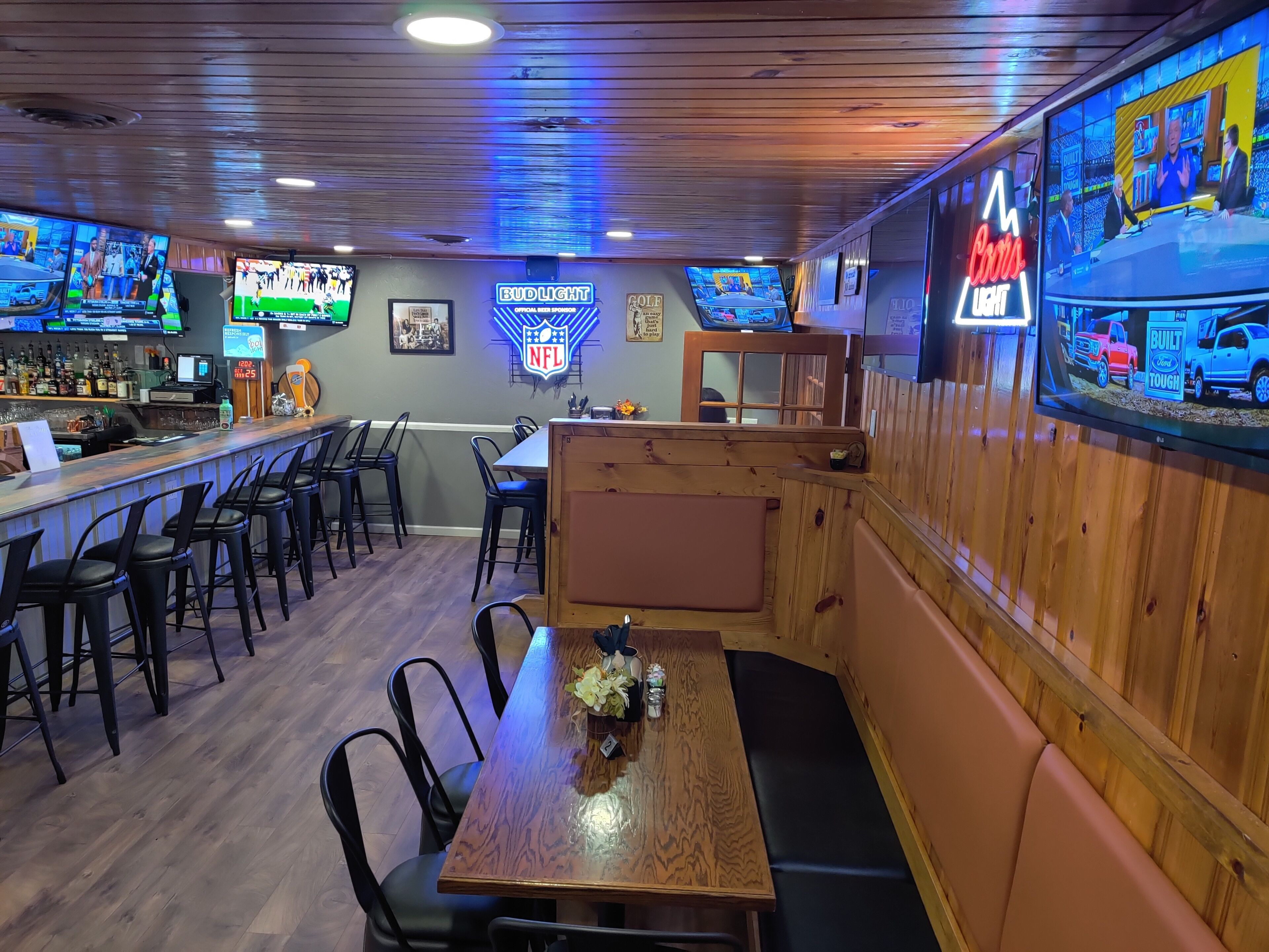Un espace bar doté de plusieurs téléviseurs, d’une enseigne publicitaire pour la bière Bud Light et d’un décor intérieur en bois.
