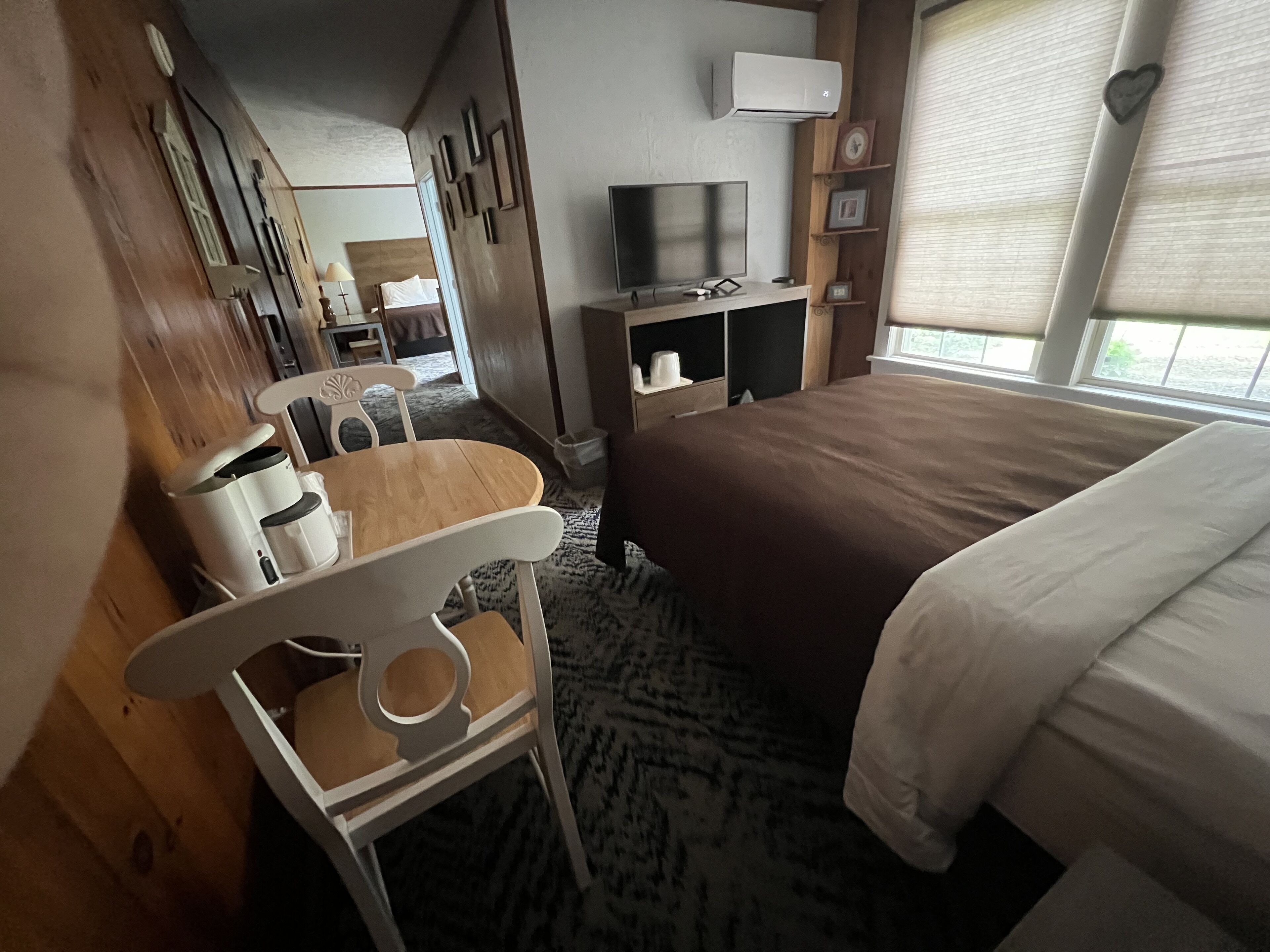 Une chambre d’hôtel avec un lit, une télévision, une petite table avec une chaise et une fenêtre avec des stores.