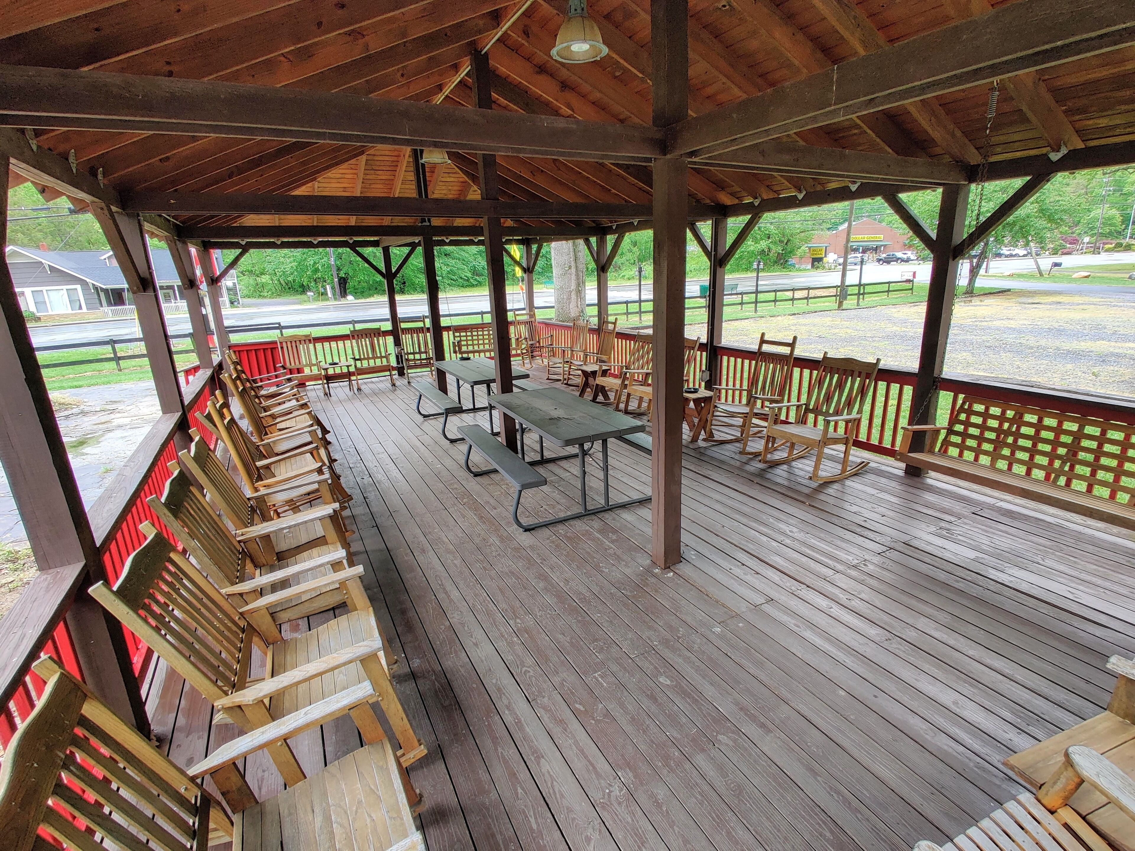 Un espace pique-nique abrité, doté de bancs et de tables en bois, d’une terrasse en bois et offrant une vue sur une route et la verdure environnante.