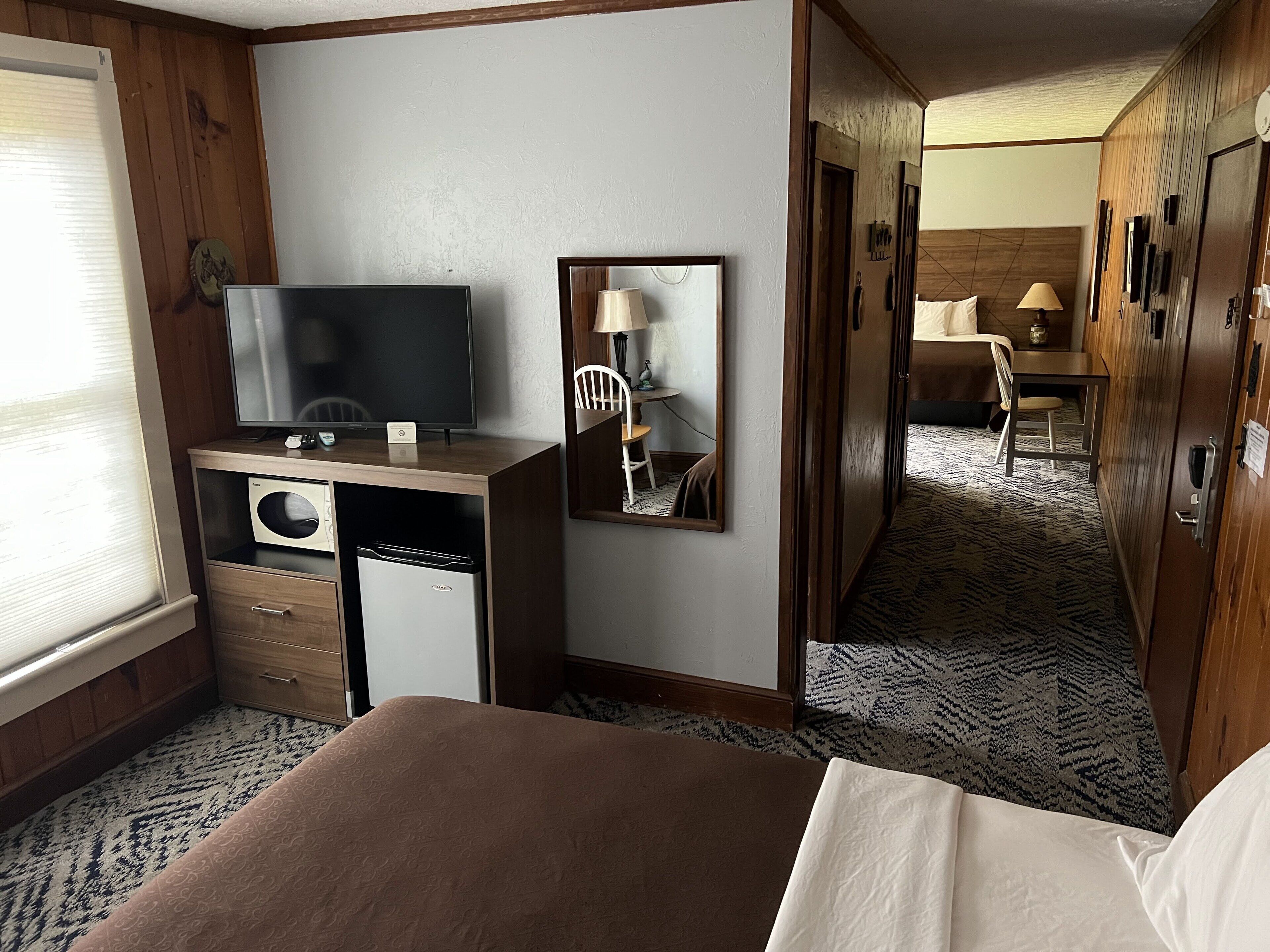 Hotelkamer met een bed, een televisie, een bureau met lamp, een spiegel en een kledingkast.