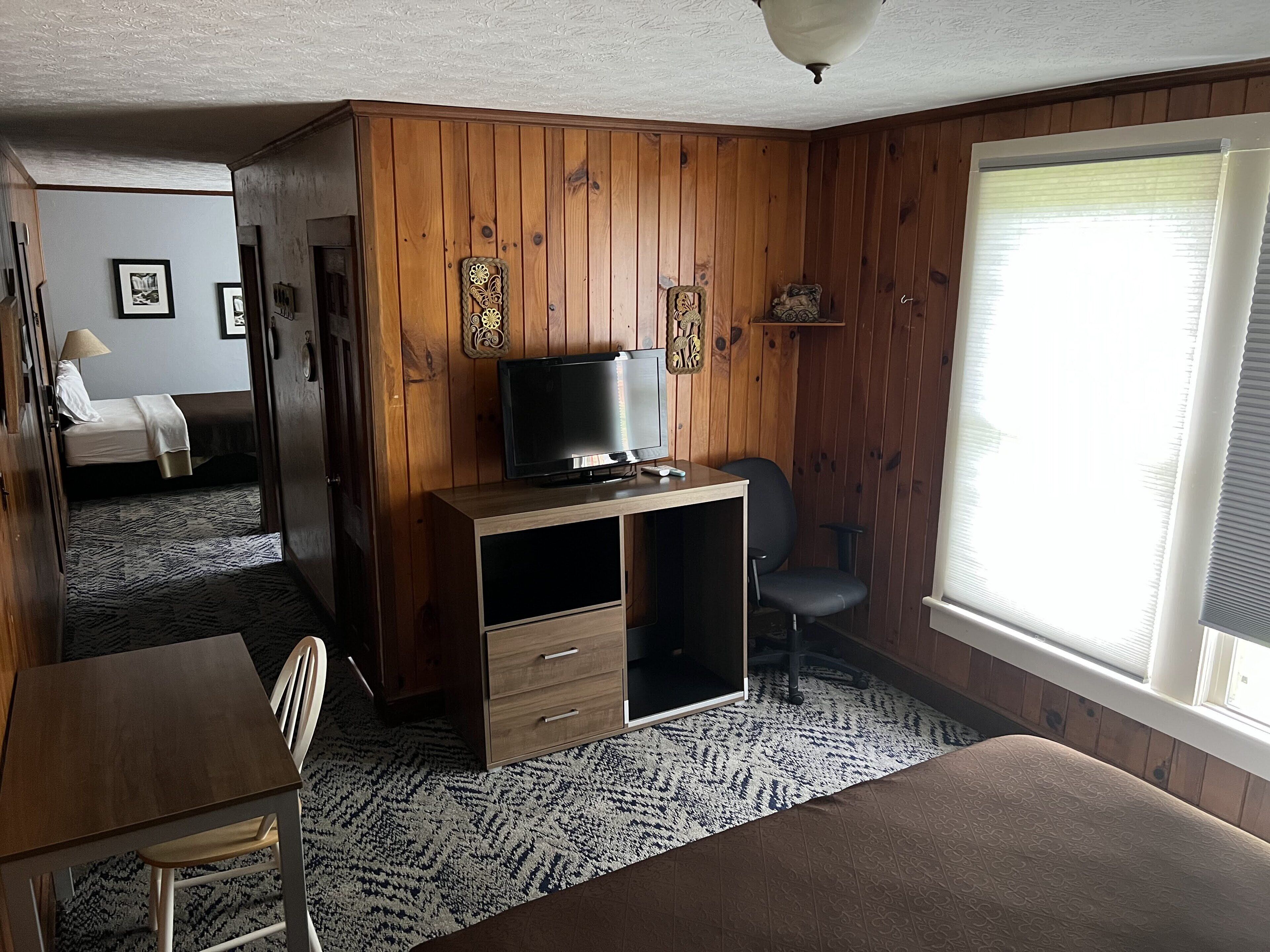 A room with wooden panel walls, a bed, a desk with a computer, a chair, and a TV.