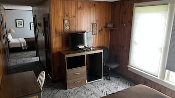 A room with wooden panel walls, a bed, a desk with a computer, a chair, and a TV.