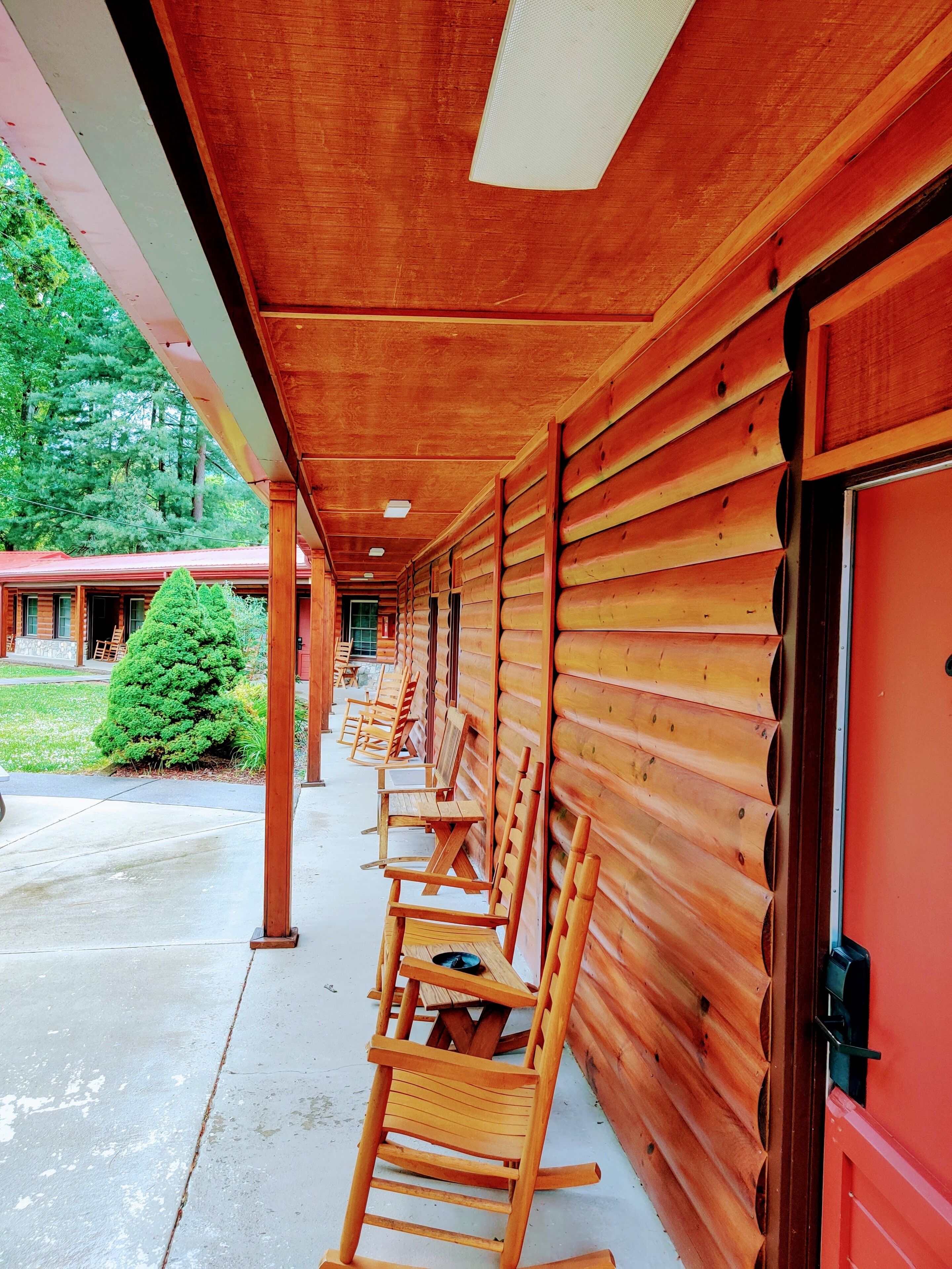 Eine Reihe aus Holzschaukelstühlen unter einer Veranda mit einer Holzfassade und einer roten Tür.
