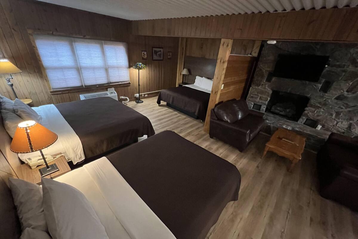 A room with two beds, a sofa, a fireplace, and a stone wall.