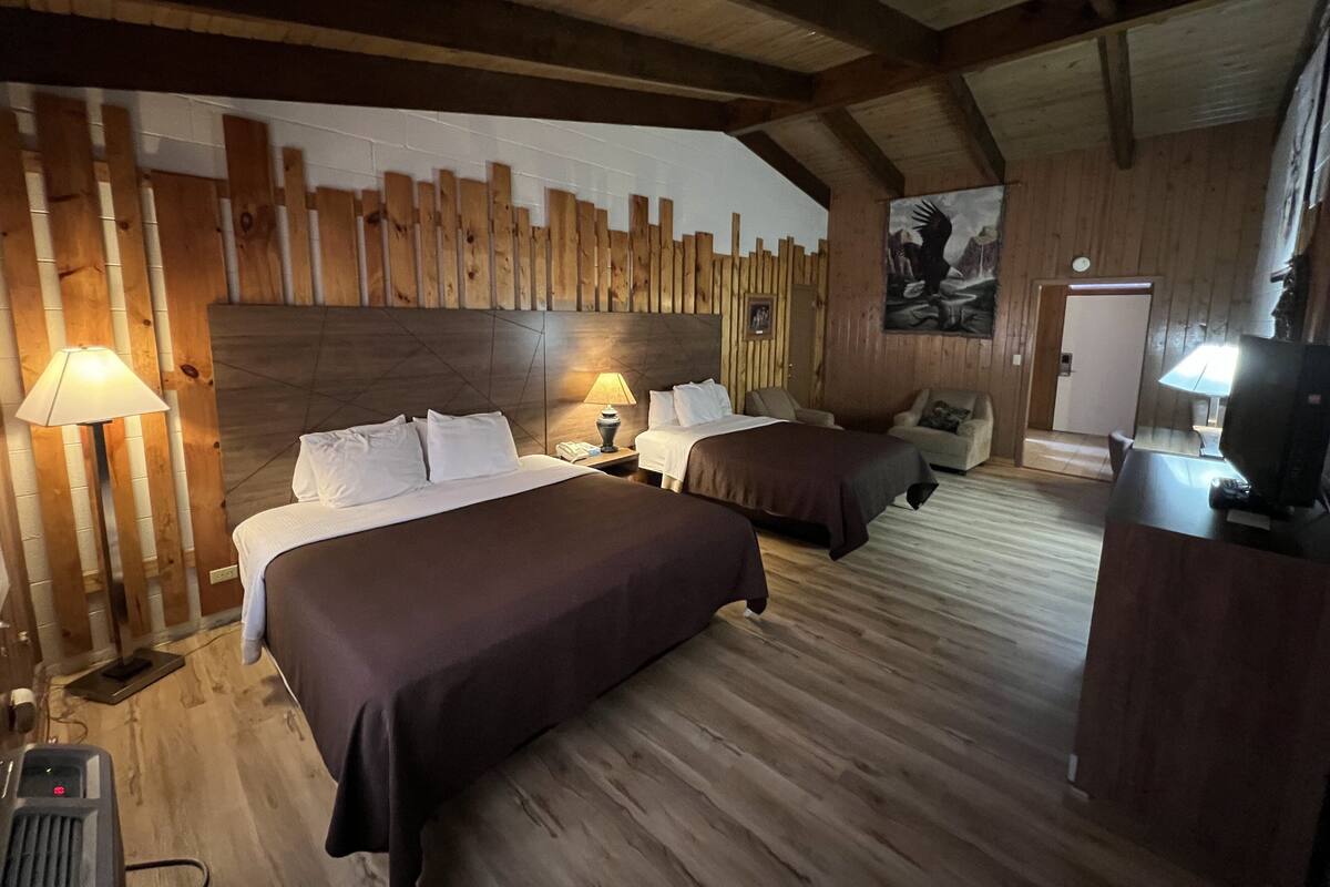 A room with two beds, wooden walls, a mounted TV, and a painting.