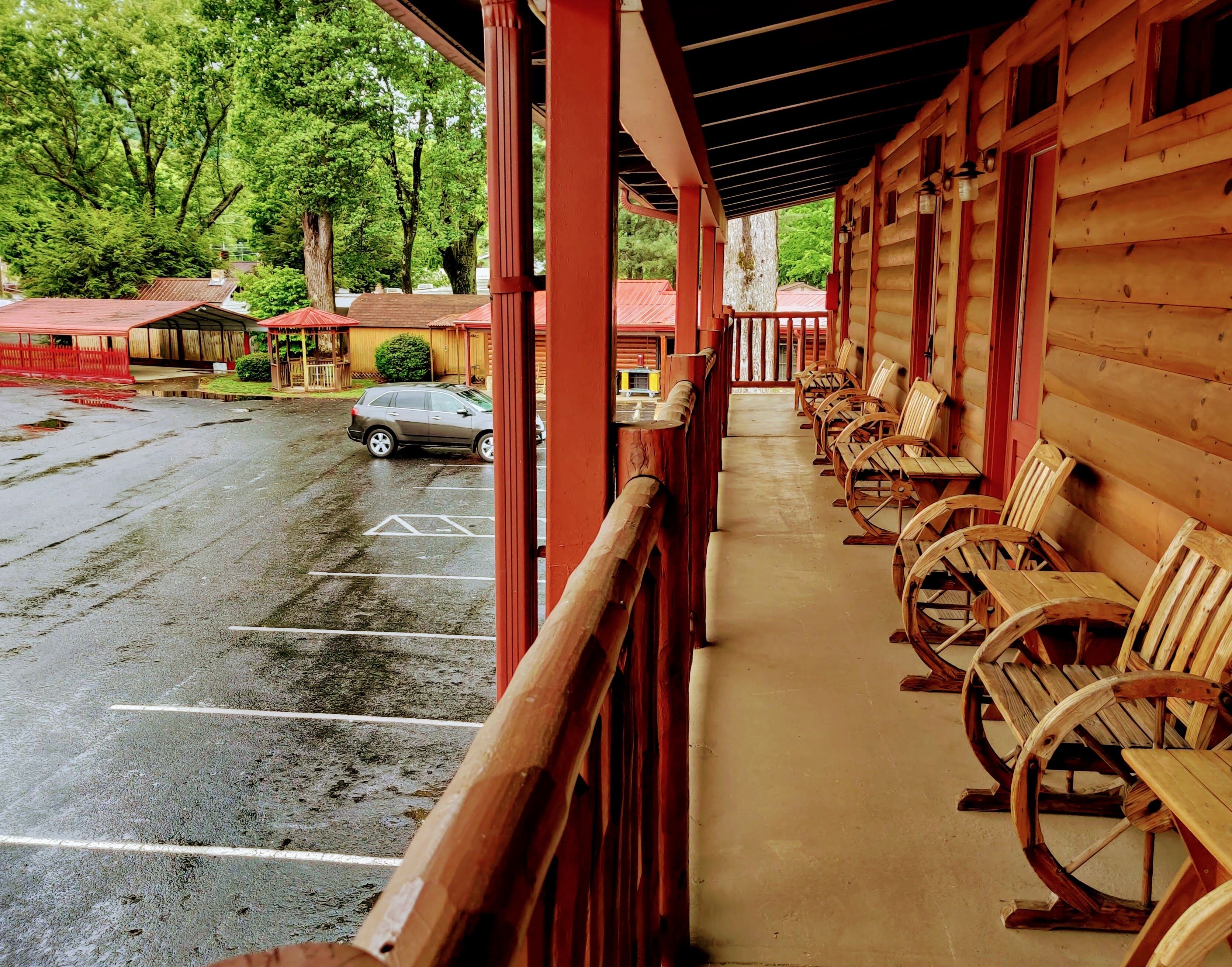 A covered porch with wooden benches and a car parked in the background.