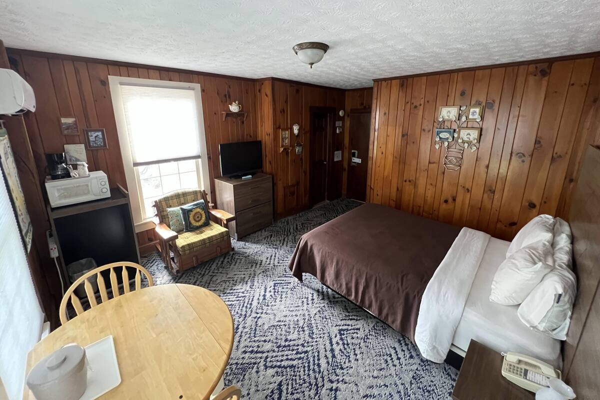 A room with a bed, a wooden table, a television, a dresser, and a window.