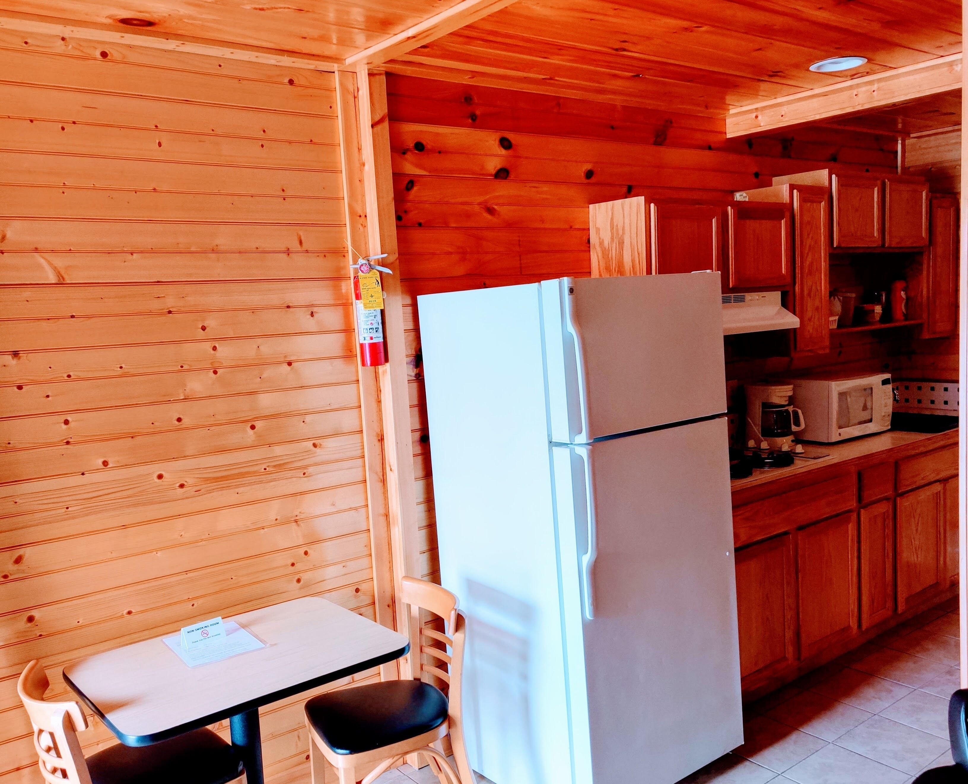 Une petite cuisine équipée avec un réfrigérateur blanc, des placards en bois, un four à micro-ondes et une table avec une chaise.