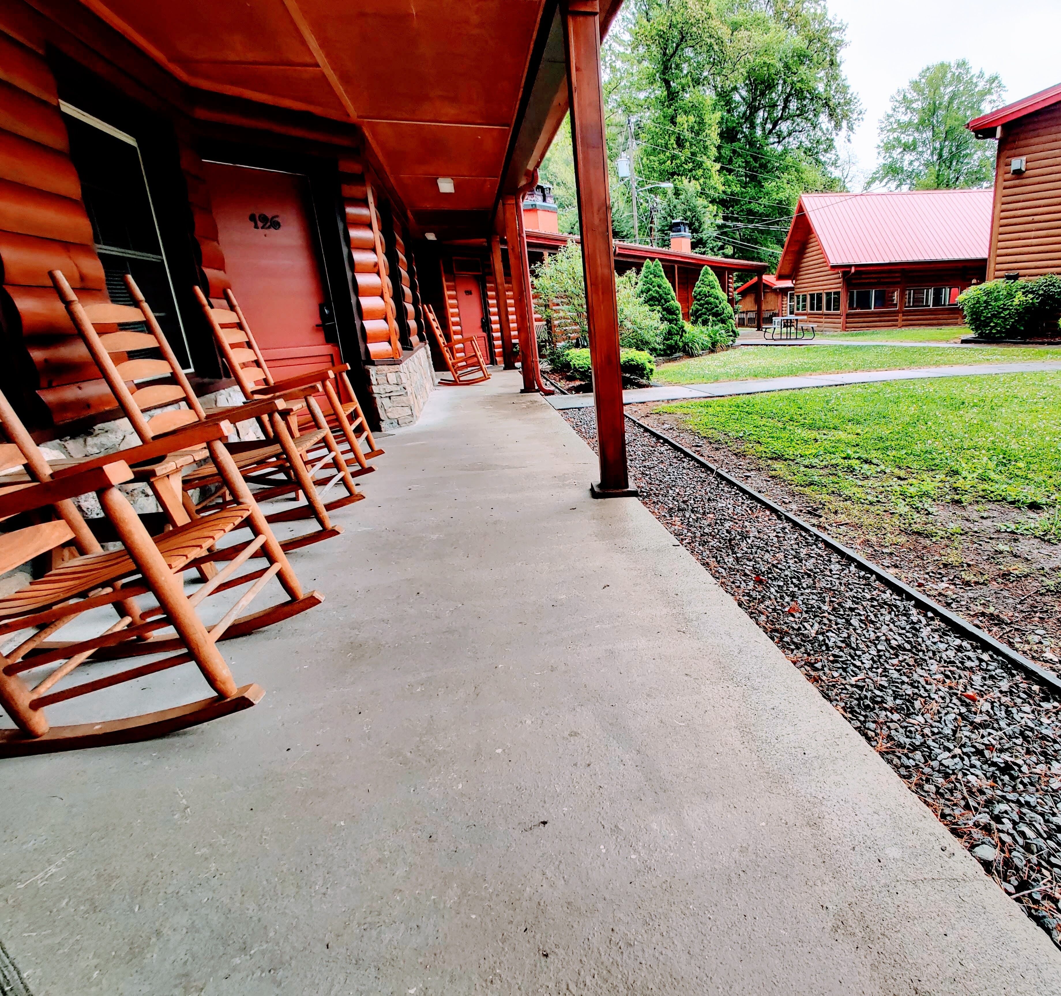 A wooden cabin with a porch lined with rocking chairs, a gravel path, and a small garden.