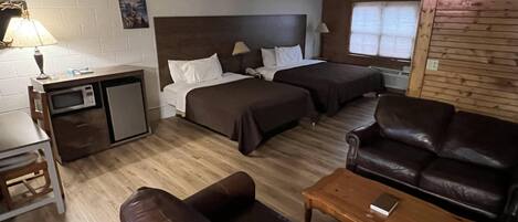 A room with two beds, a desk with a lamp, a leather sofa, and a wooden coffee table.