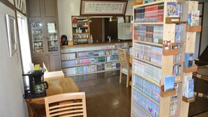 A library with wooden bookshelves, a coffee machine, and a counter with various items. - Pension Megumiyuki (Biei)
