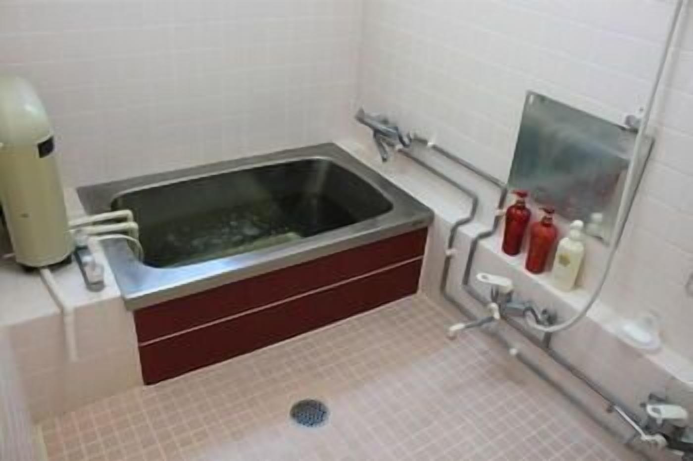 Un baño con un lavamanos rectangular, un espejo y dos botellas rojas en la pared.