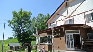 A building with a wooden exterior and a white door, a bench, and picnic tables in front. - Pension Megumiyuki (Biei)